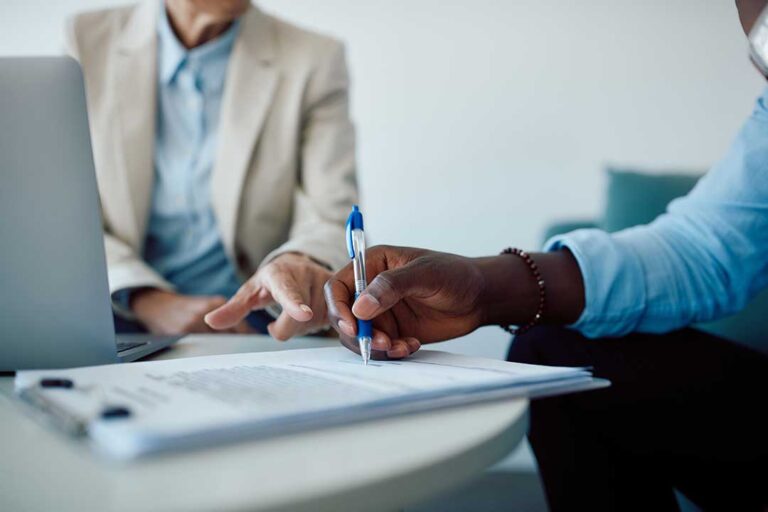 Two adults sit at a kitchen table looking over insurance policy documents together.