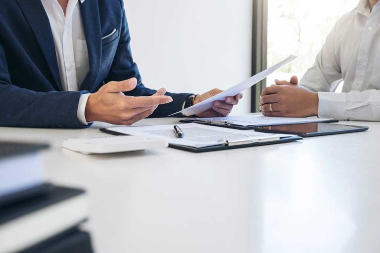 Family reviews insurance documents at a kitchen table beside a home, car keys, and a calculator.